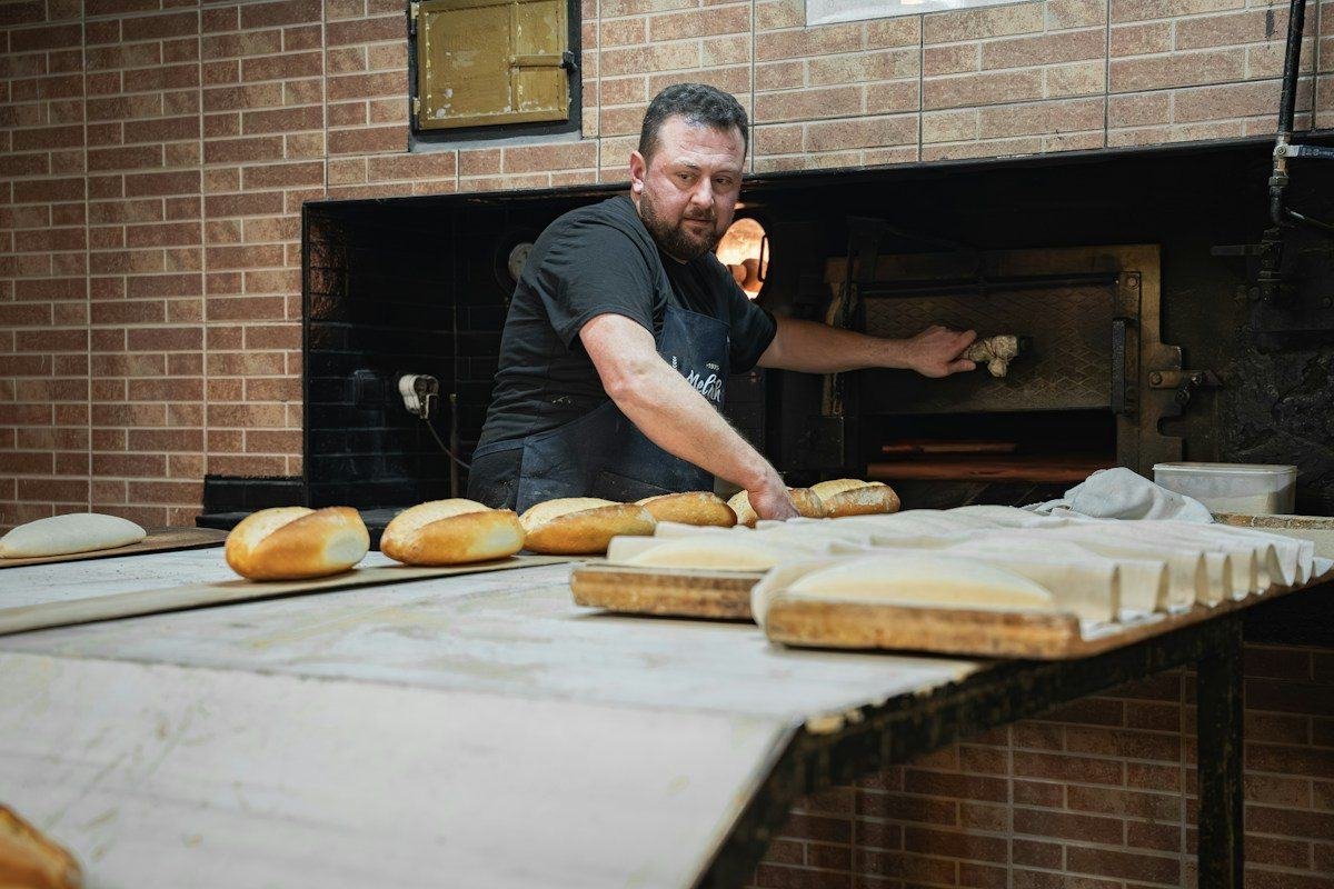 A baker pulling fresh bread from a modern oven