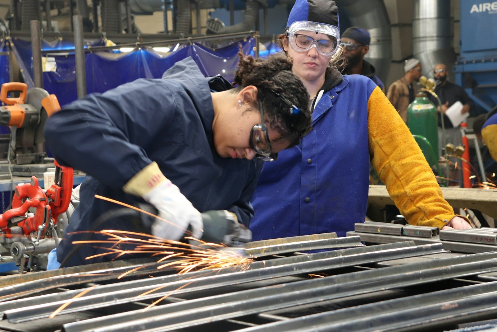 An instructor coaching a trainee in a metal workshop